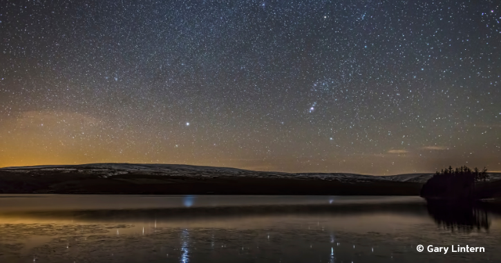 View of a starry night sky reflected in the water of Burnhope Reservoir County Durham..